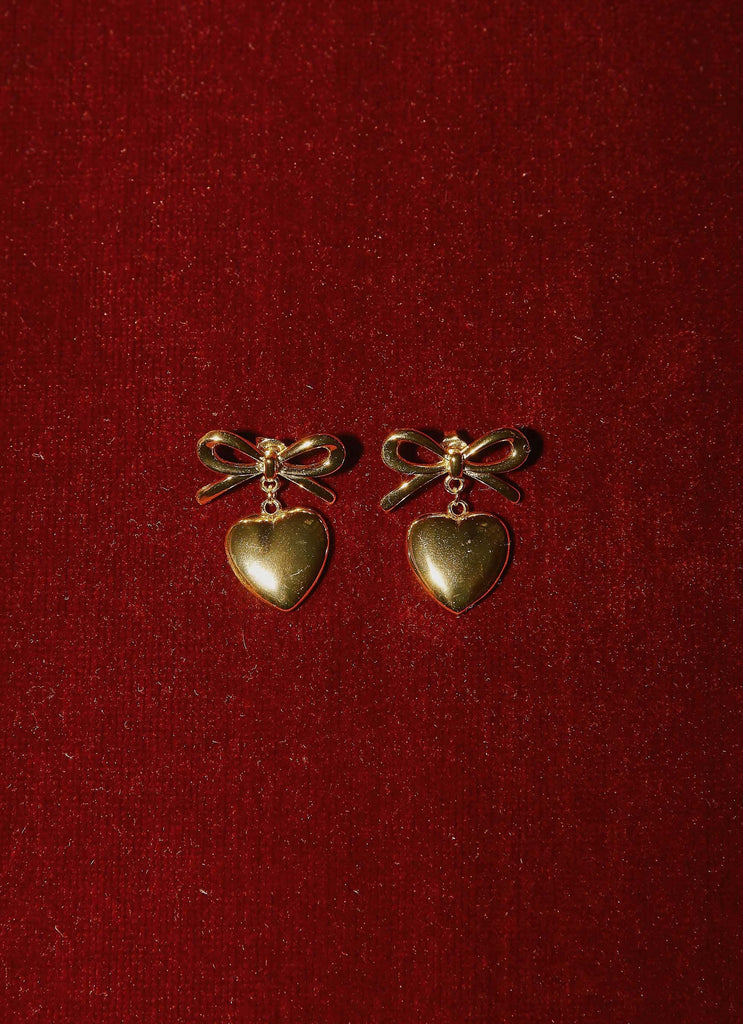 Womens Chasity Bow And Heart Earrings in the colour Gold in front of a light grey background