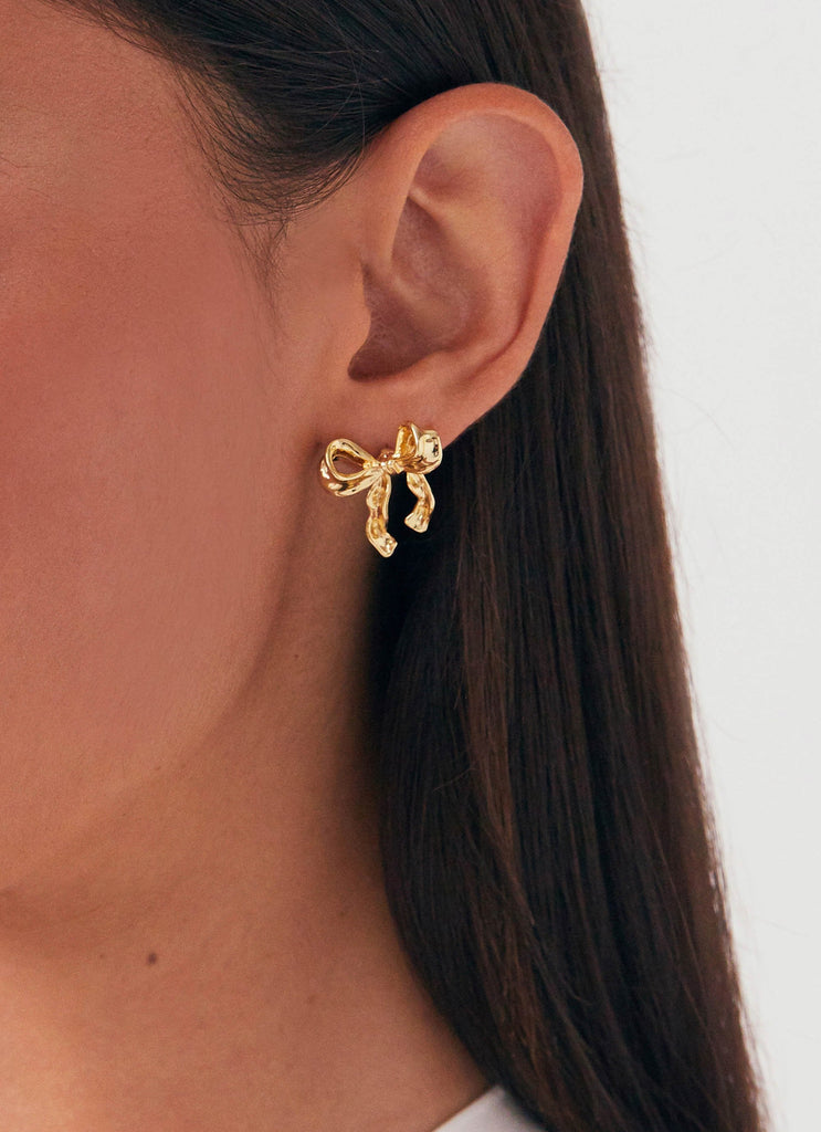 Womens Kindra Mini Bow Earring in the colour Gold in front of a light grey background