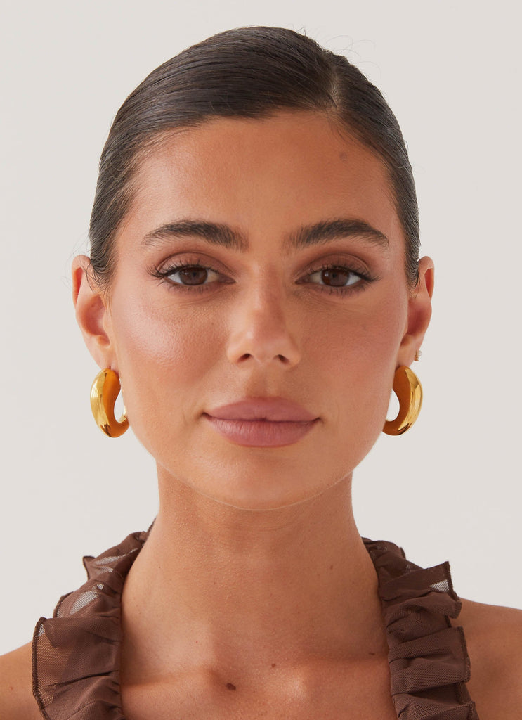 Womens Glow Girl Hoop Earrings in the colour Gold in front of a light grey background