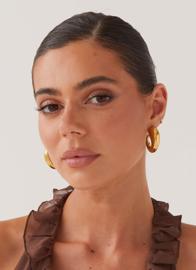 Womens Glow Girl Hoop Earrings in the colour Gold in front of a light grey background